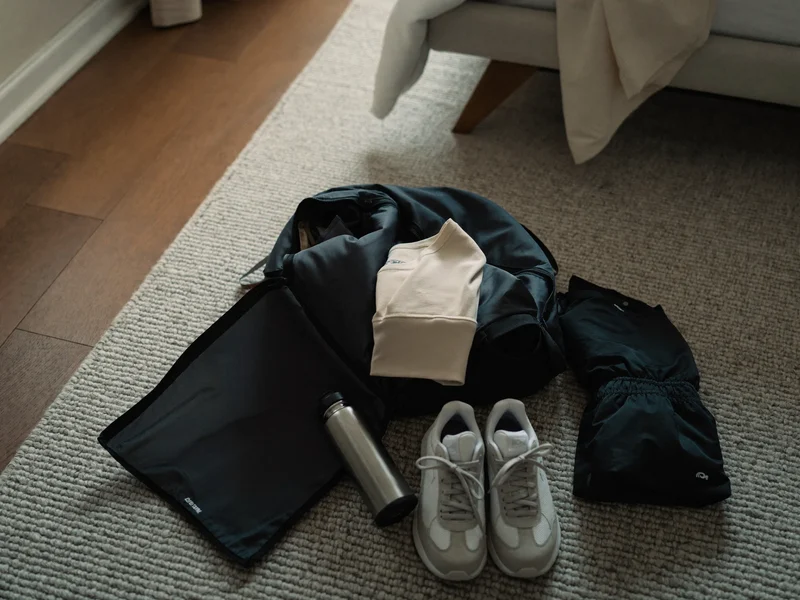 Åben duffeltaske pakkes på soveværelsesgulv med sportstøj, drikkedunk og sneakers